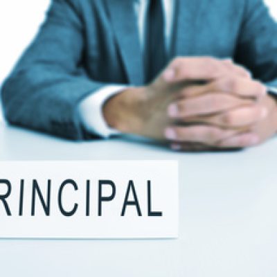 a man wearing a suit sitting in a desk with a signboard in front of him with the word principal written in it